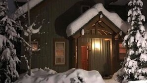 Une cabane en bois, avec un toit enneigé et une porte en bois.