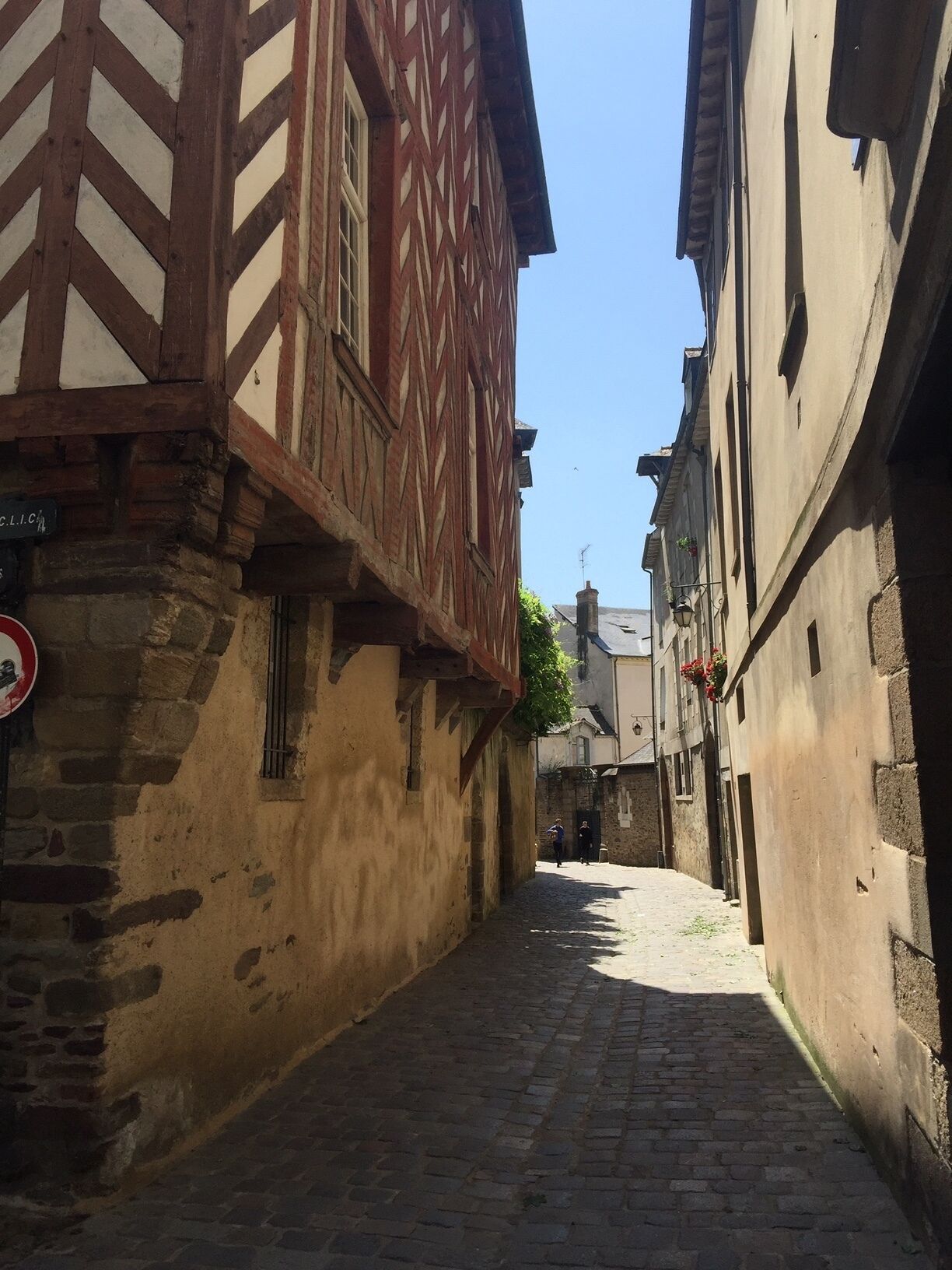 A narrow cobblestone street flanked by historic buildings with timber framing and stone walls.