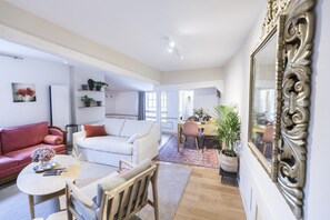 Un vaste espace de vie comprenant un canapé rouge, un canapé blanc et une table à manger avec des chaises. On y trouve également des plantes en pot et un grand miroir accroché au mur.