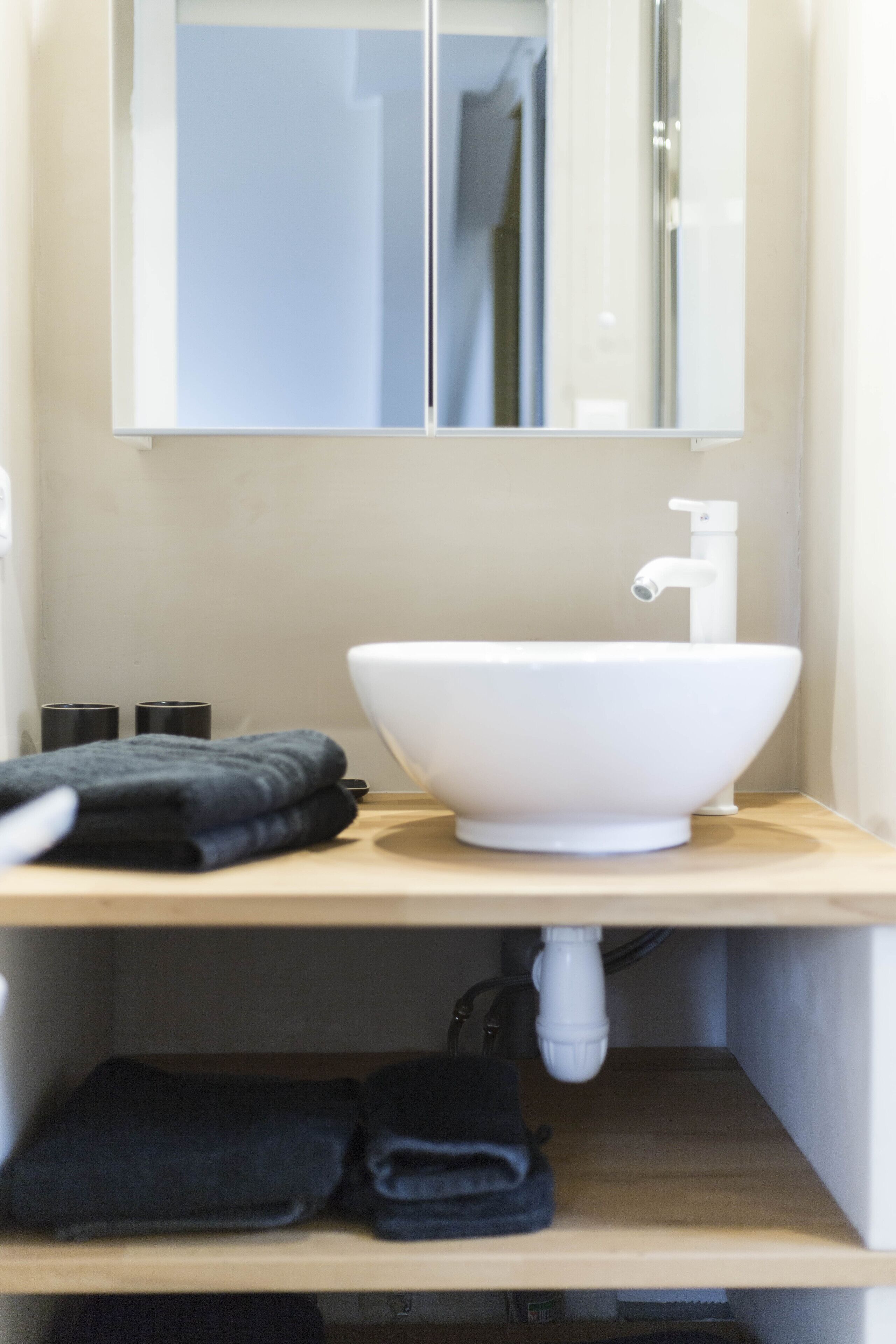 Un baño con un lavamanos blanco, un espejo encima y un perchero con toallas dobladas.