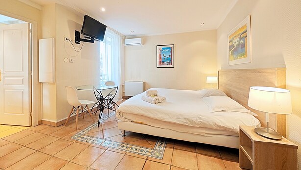 A hotel room with a bed, a desk, a chair, a TV, and a painting on the wall.