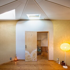 A spacious room with a sloped ceiling, a skylight, a wooden door with a decorative pattern, a floor lamp, and a small table with a basket. - Twin Dome Ryugu (Hokuto)