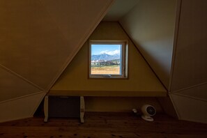 A room with a sloped ceiling, a window with a mountain view, a radiator, and a fan on the floor. - Twin Dome Ryugu (Hokuto)