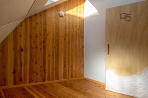 A room with wooden panel walls, a sloped ceiling, and a door with a decorative panel. - Twin Dome Ryugu (Hokuto)
