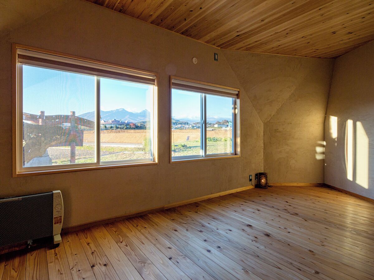 A room with wooden floors, two large windows with a view of a landscape, and a radiator on the wall.