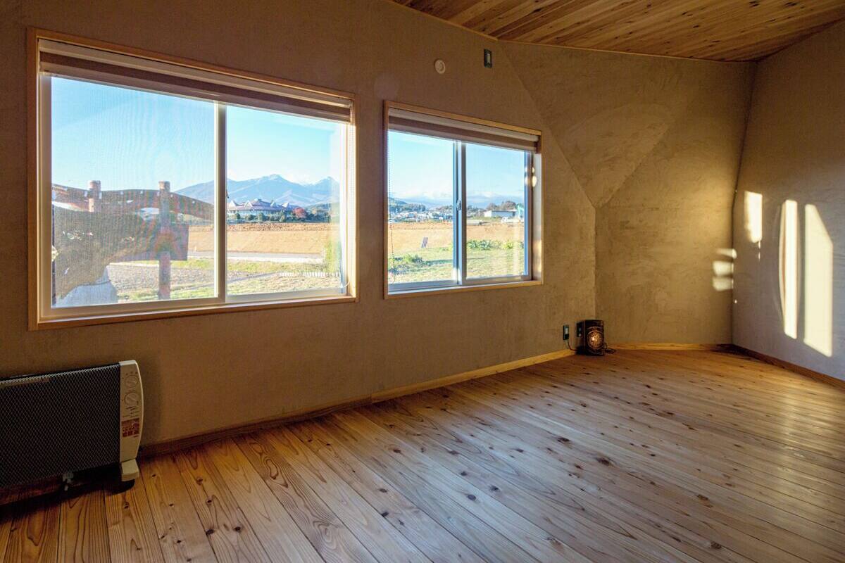 A room with wooden floors, two large windows with a view of a landscape, and a radiator on the wall.