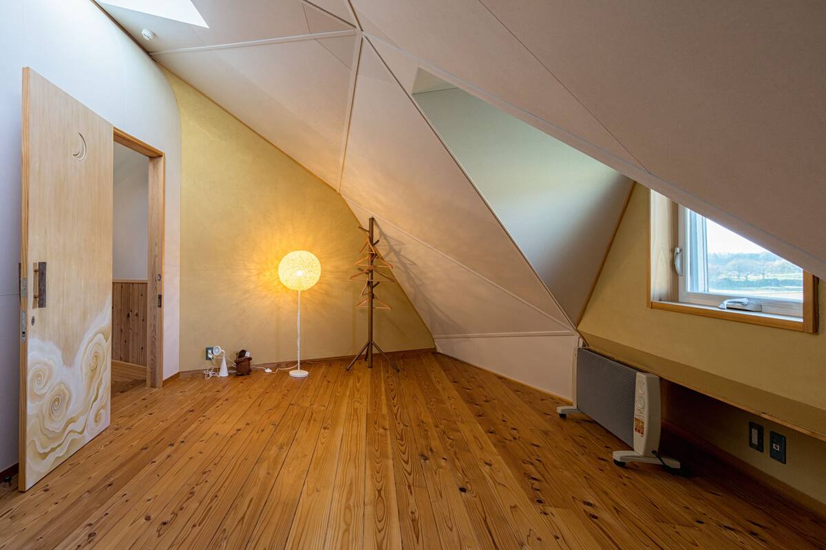A room with wooden flooring, a standing lamp, a tripod, and a window with a view.