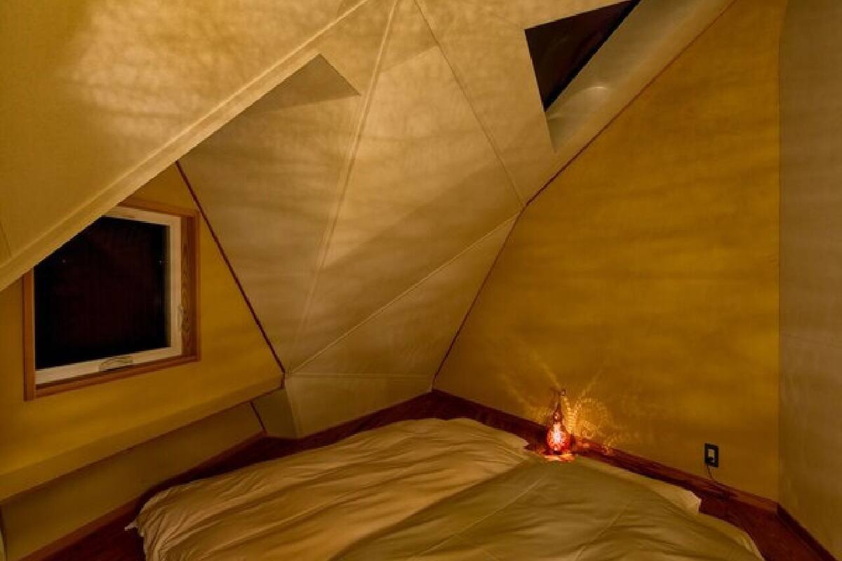 A triangular attic bedroom with a single window, a bed, and a visible electrical outlet.