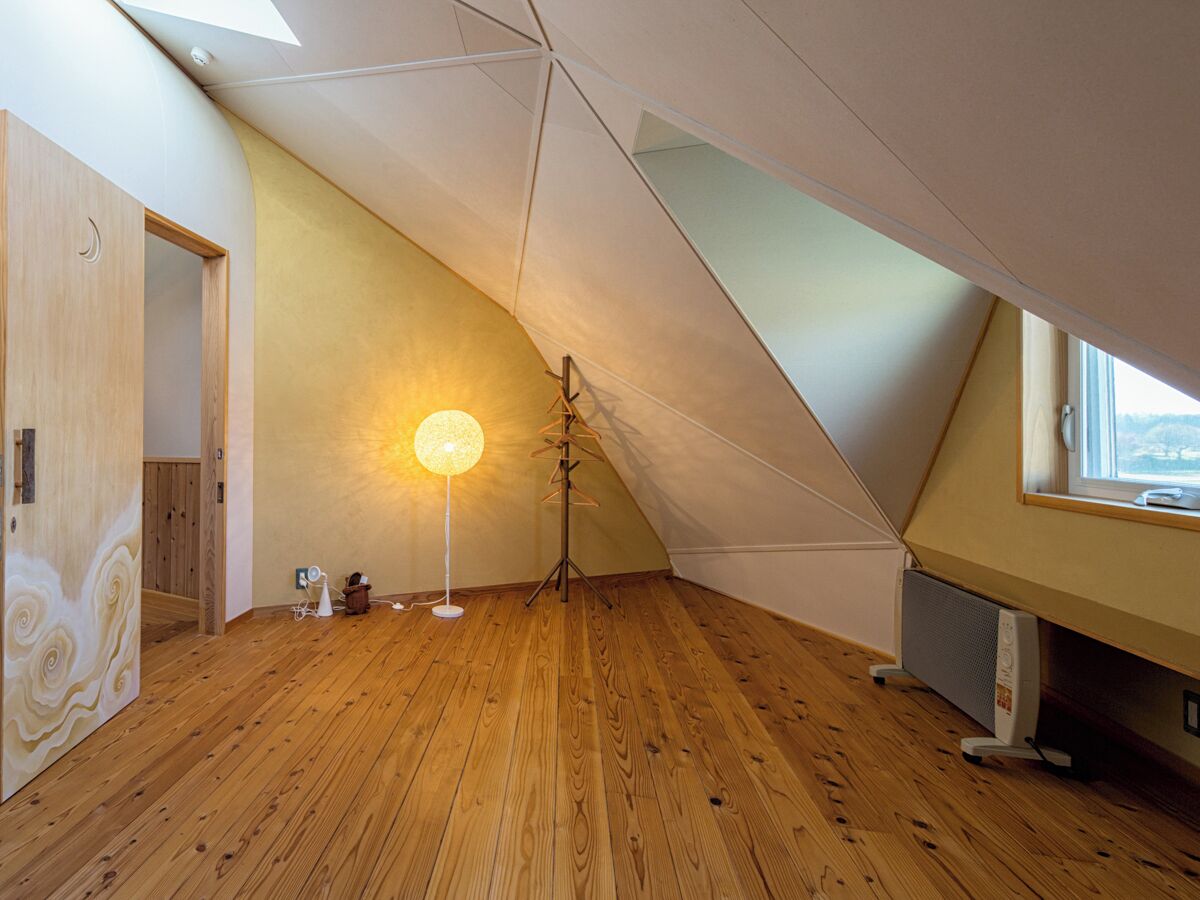 A room with wooden flooring, a standing lamp, a radiator, and a window with a view.