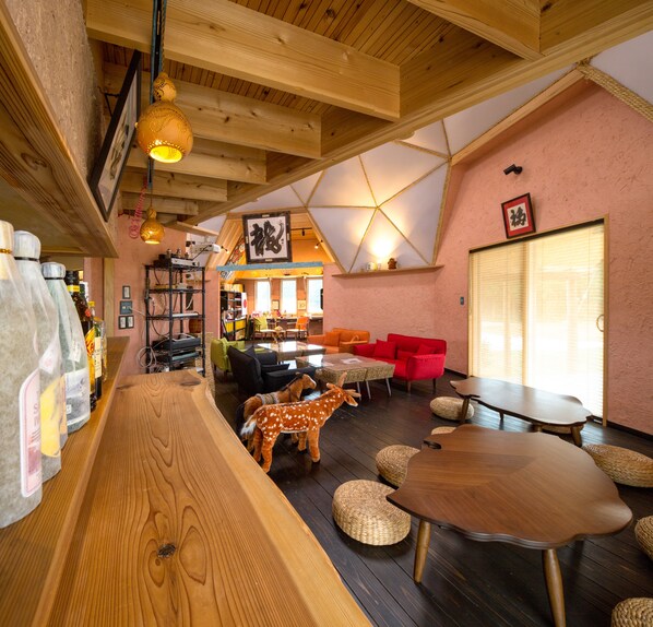 A cozy interior with a wooden bar, plush seating, and a high ceiling with exposed beams.