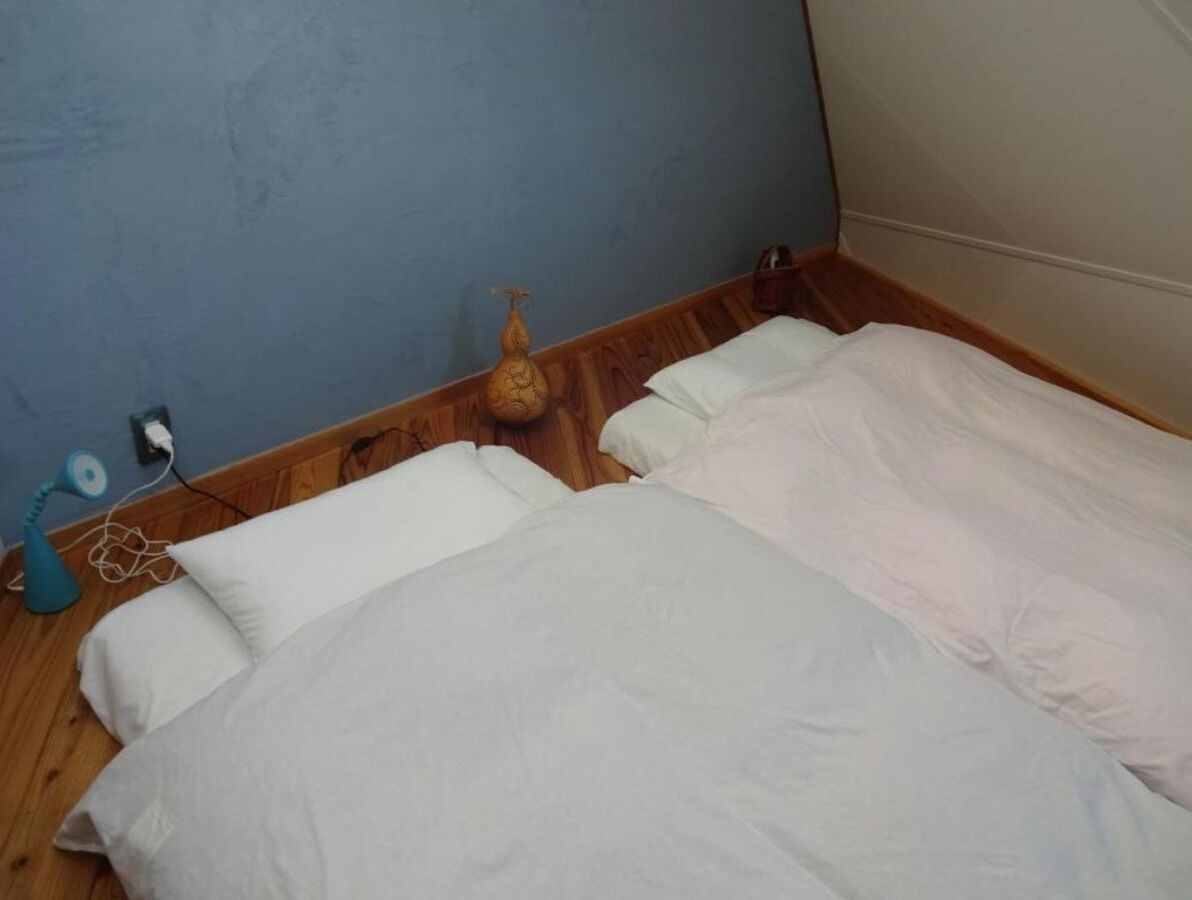 Ein Zimmer mit zwei Betten, Holzboden, einer blauen Wand und einem kleinen Tisch mit einer Lampe.