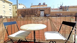 En takterrass med två stolar och ett bord, med utsikt över en stadssiluett med byggnader och en klar himmel.