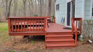 A wooden deck with a bench and a chair, leading to a house with a sliding glass door.