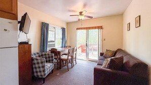 A compact living space with a dining area, a couch, a ceiling fan, and a sliding glass door leading to an outdoor deck.