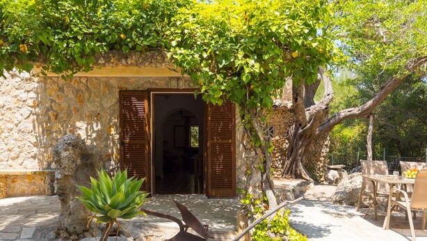 A stone building with wooden shutters, a stone pathway, and a table with chairs outside. - Can Company - Beautiful finca with pool and garden in Campanet (Campanet)