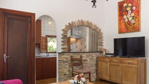 A kitchen with a stone arch, wooden cabinets, a TV, and a dining table with a basket of flowers. - Can Company - Beautiful finca with pool and garden in Campanet (Campanet)