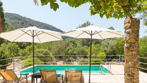 A pool area with three umbrellas, a stone pillar, and a view of a mountainous landscape. - Can Company - Beautiful finca with pool and garden in Campanet (Campanet)