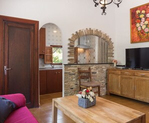 Una cocina con arco de piedra, armarios de madera, un televisor y una mesa de comedor con un cesto de flores.