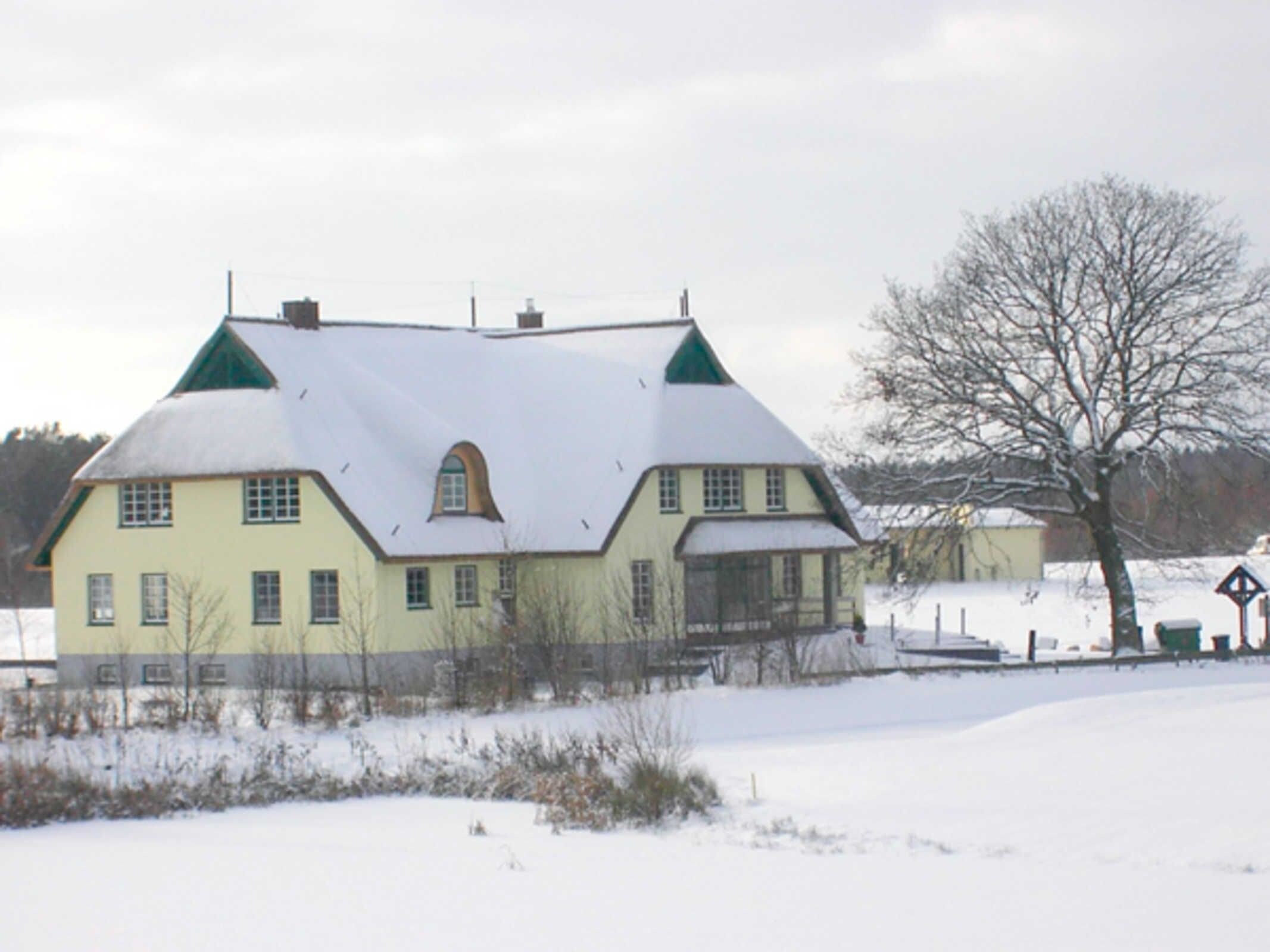 Una casa grande de dos pisos con techo pronunciado, múltiples ventanas y un paisaje cubierto de nieve.