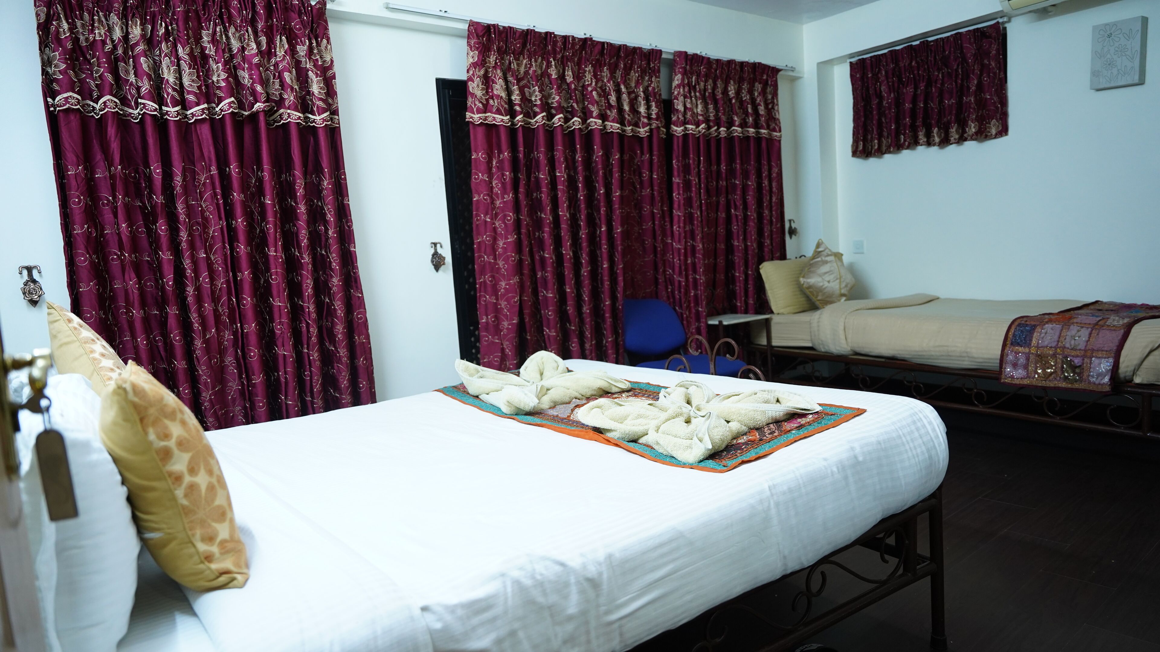 A hotel room with a single bed, a chair, and two windows with red curtains.
