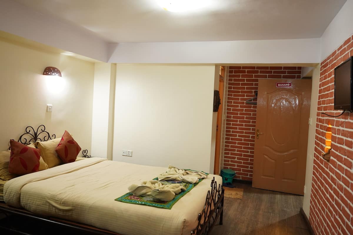 A hotel room with a bed, a nightstand, a wall-mounted TV, and a door leading to another room.