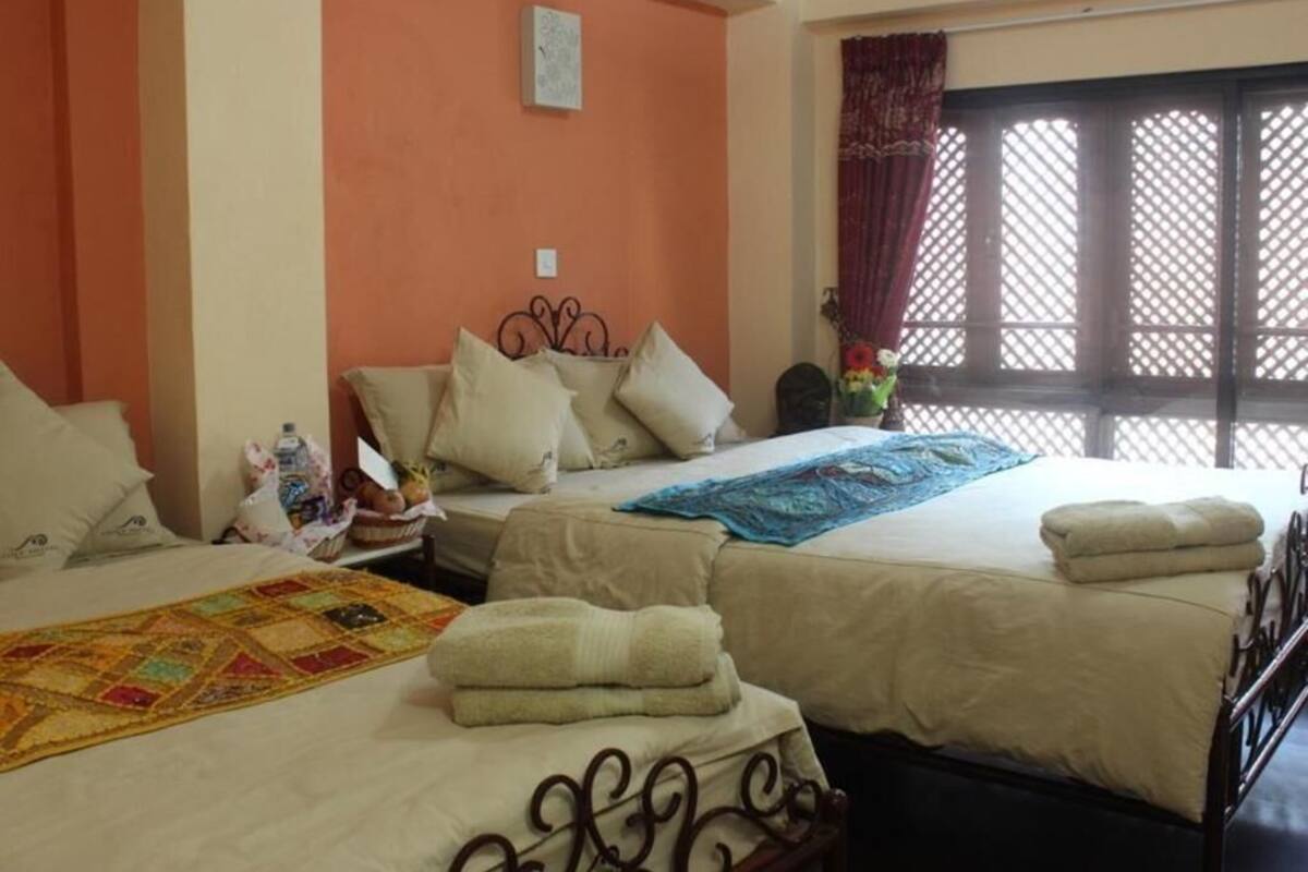 A hotel room with two beds, a window with a lattice screen, and a quilt on the floor.