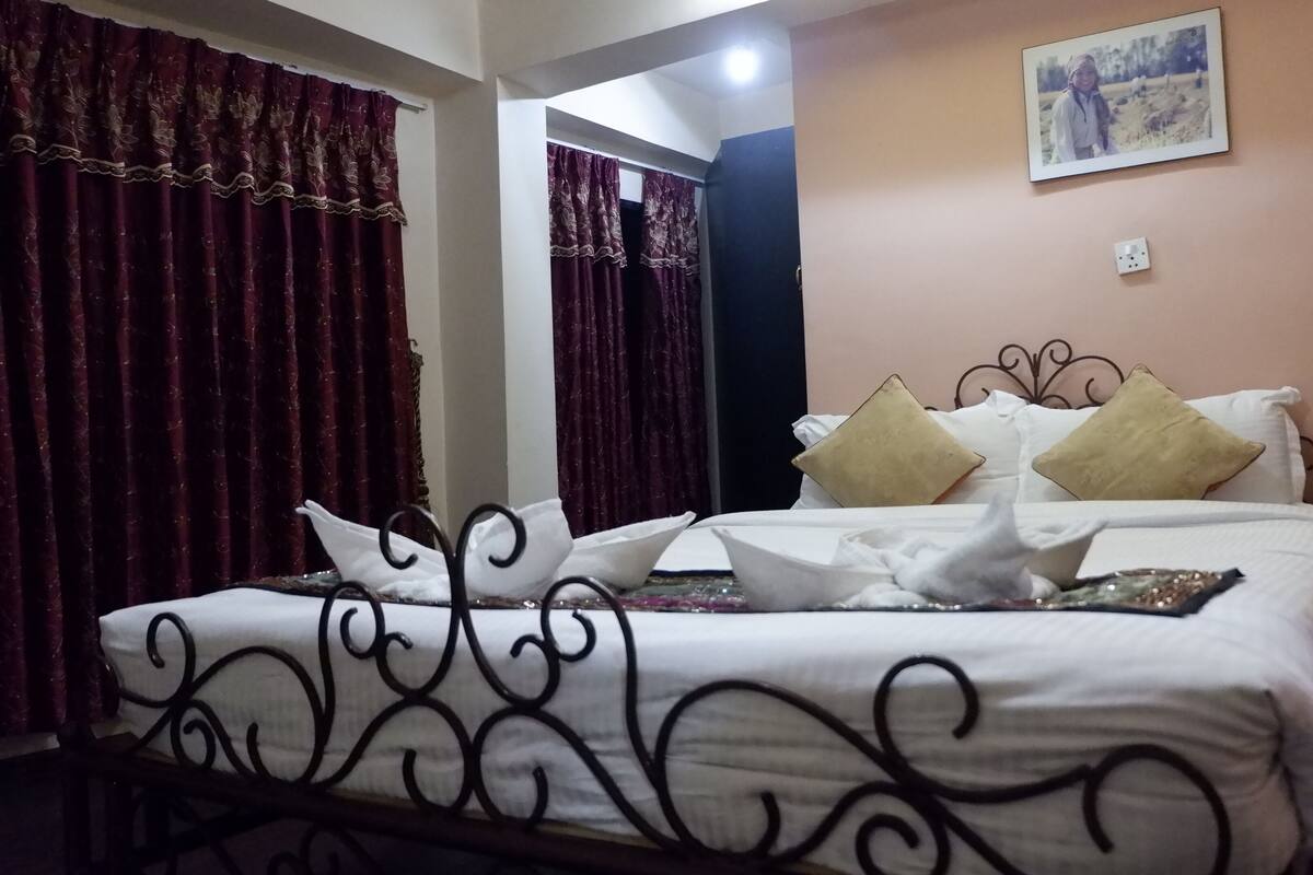 A neatly made bed with white linens and decorative pillows, a bedside table with a lamp, and a framed photo on the wall.