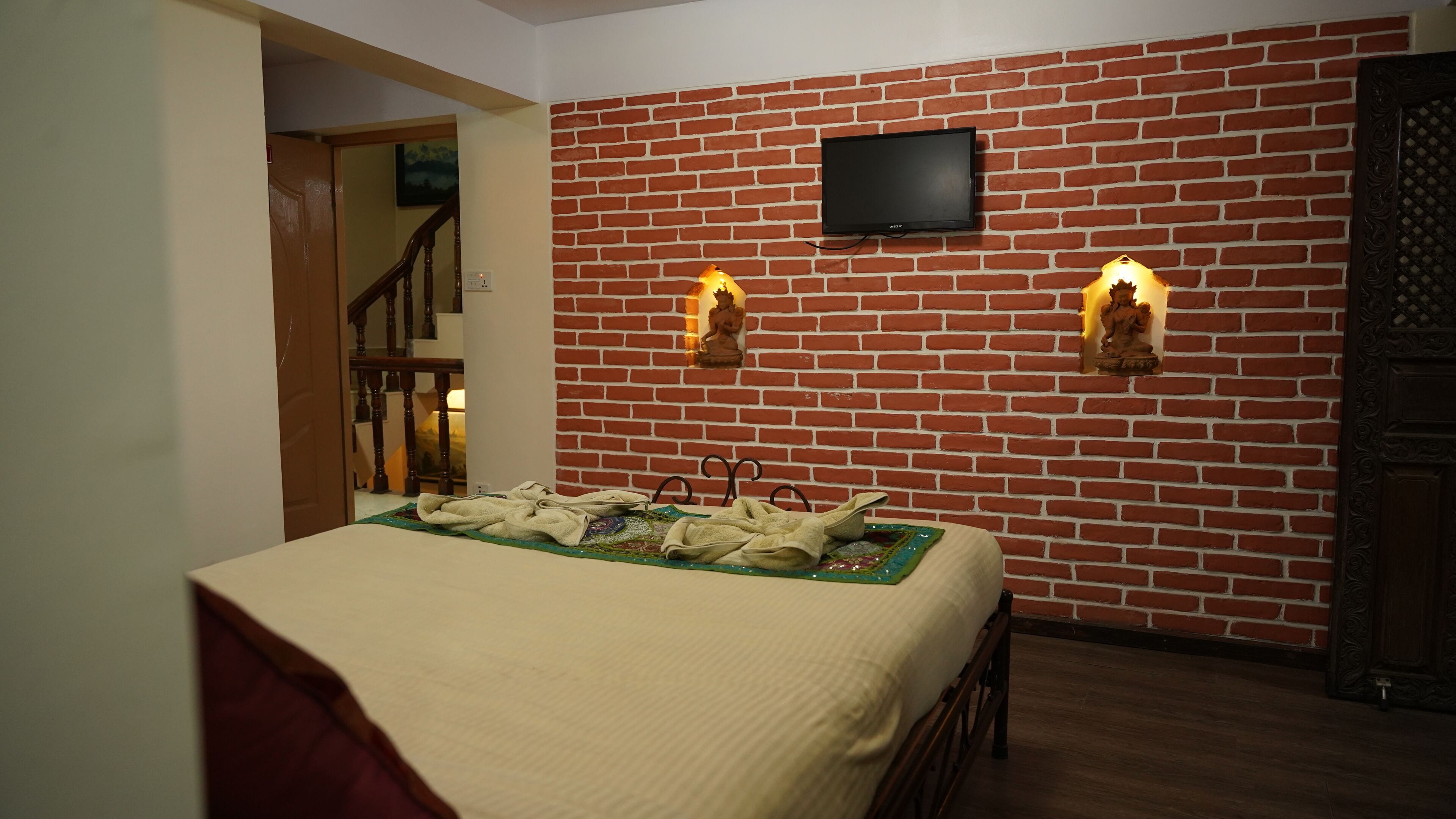 Una habitación con pared de ladrillo, cama con colchoneta verde y dos luces fijadas a la pared.