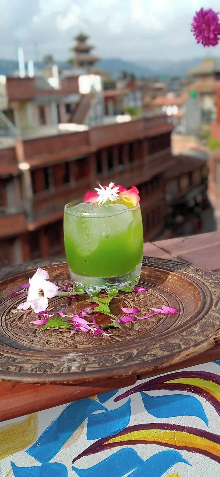 Una bebida verde sobre un plato decorativo, con un paisaje urbano de fondo.