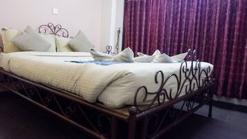 A neatly made bed with a white duvet and multiple pillows, a dark metal bed frame, and a purple curtain in the background.