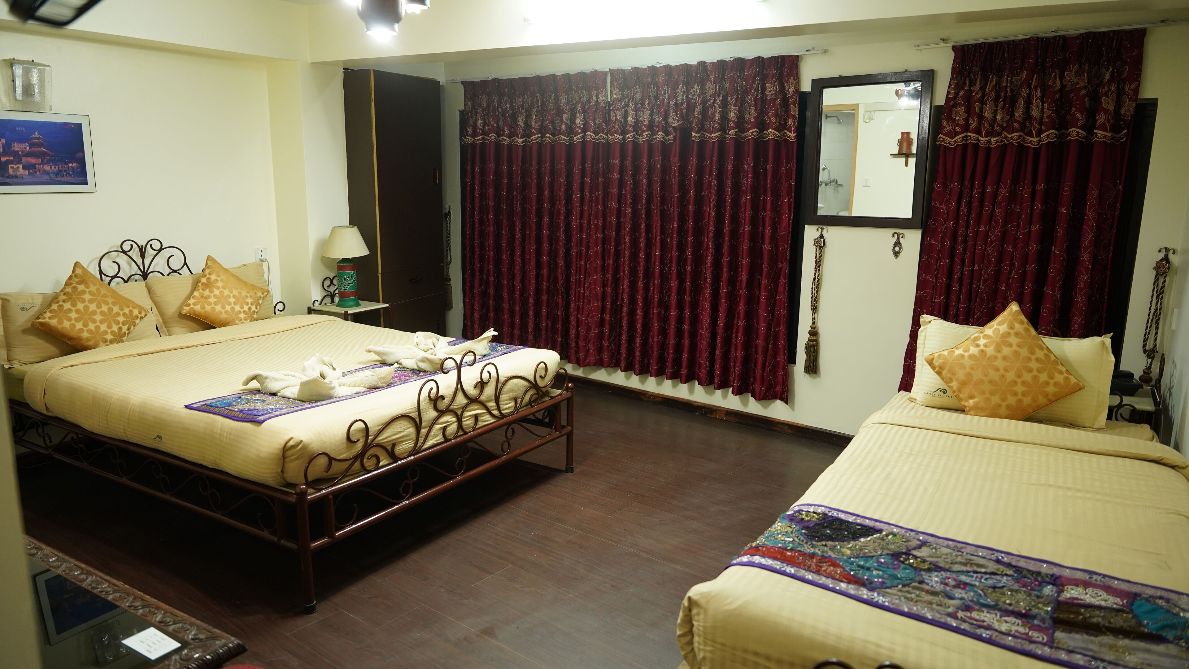 A hotel room with two beds, a wardrobe, a mirror, and a bathroom visible through a door.