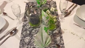 Une table à manger dressée avec des assiettes, des couverts, des verres et des éléments décoratifs, notamment un pichet en verre et des compositions florales.