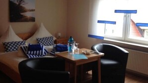 Une pièce comprenant un lit, deux chaises, une table avec une bouteille et un verre, et une fenêtre avec des stores.