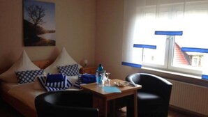 Une pièce comprenant un canapé, deux fauteuils, une petite table, une fenêtre avec des stores et un tableau accroché au mur.