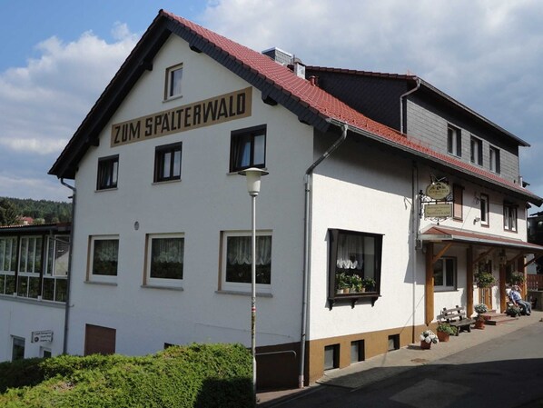 Un bâtiment à deux étages, sur lequel on peut lire l’inscription « Zum Spalterwald », ce qui indique qu’il s’agit d’un hôtel. Il y a des fenêtres aux deux étages, un lampadaire et un banc à l’extérieur.