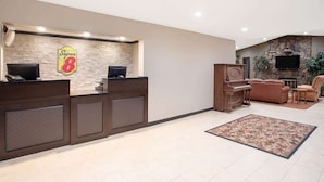 A reception area with a stone wall, a Super 8 sign, a reception desk, a piano, sofas, and a TV. - Super 8 Billings (Billings)