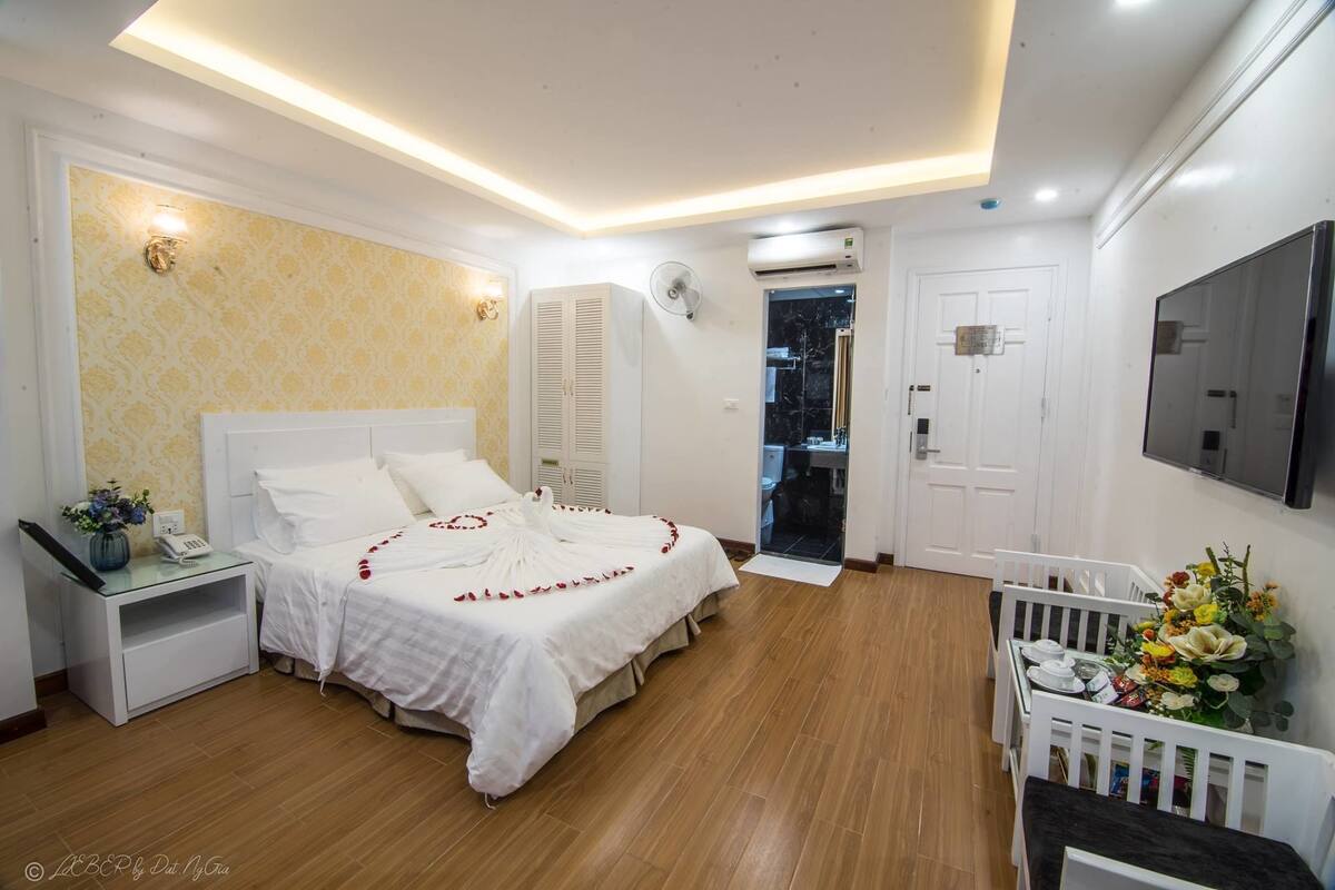 A bedroom with a bed, bedside table, air conditioning unit, and a TV mounted on the wall.