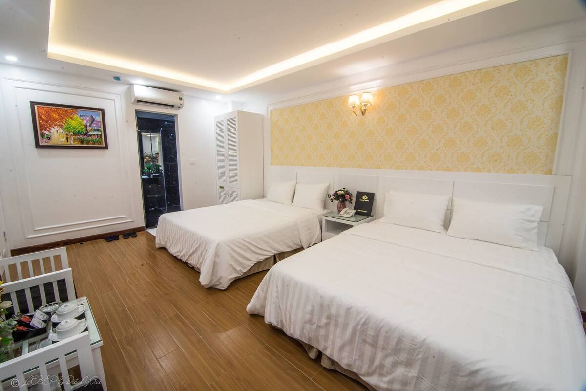 A hotel room with two single beds, a small table with a vase, and a wall-mounted air conditioner.