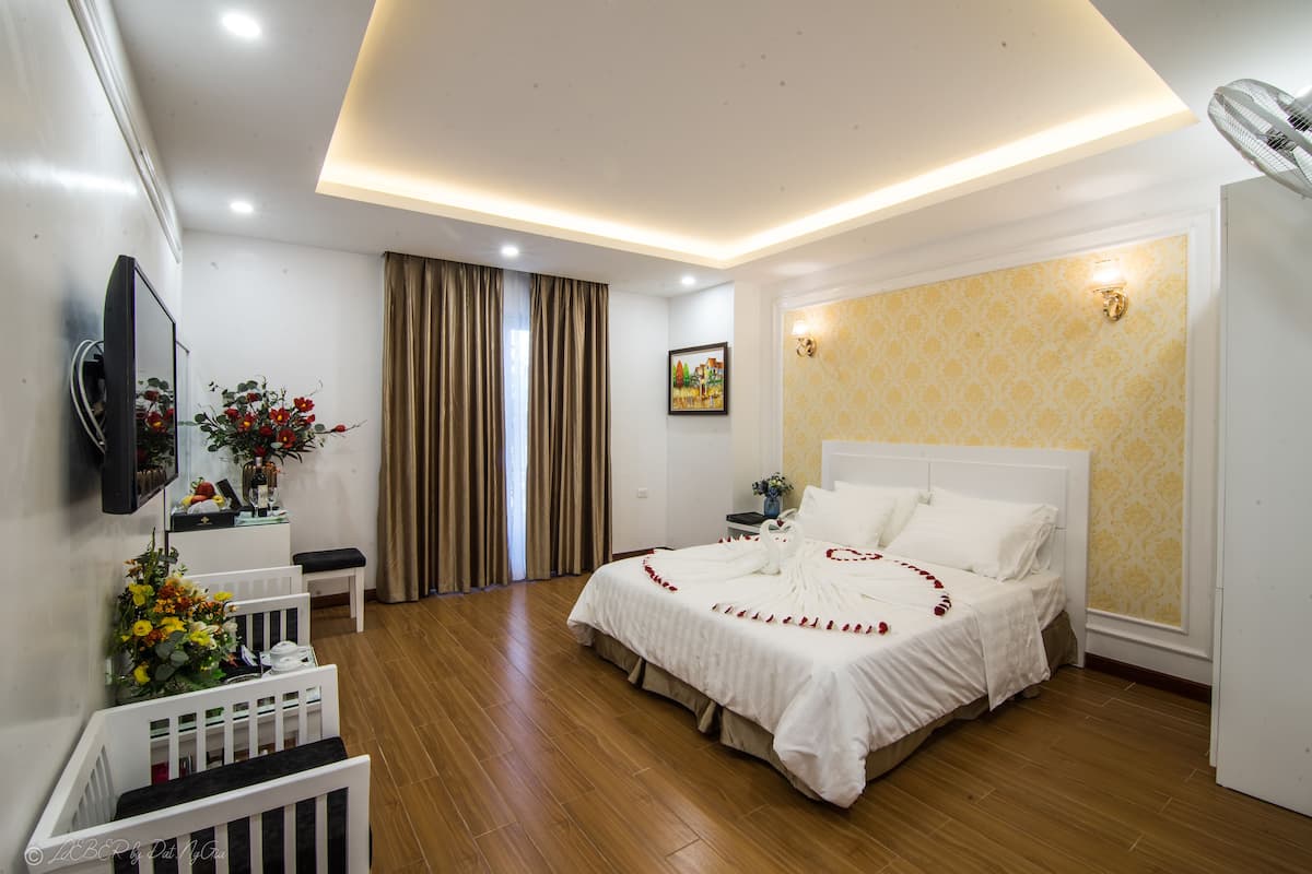 A hotel room with a large bed, a television, a desk with a chair, and a window with curtains.