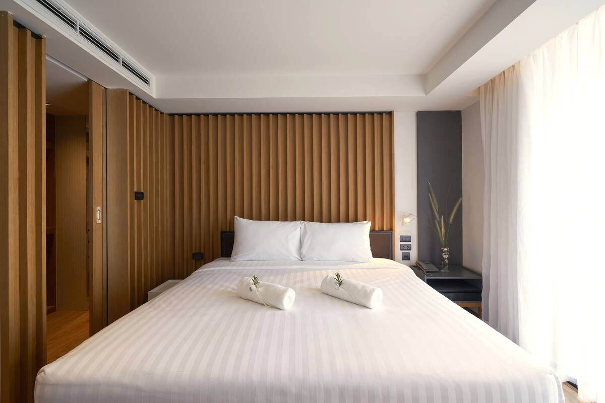 Une chambre d’hôtel avec un grand lit, des murs lambrissés, une table de chevet avec une lampe et une vue sur l’extérieur.