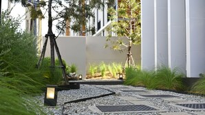 Een pad met decoratieve verlichting, omringd door grind en planten, dat leidt naar een gebouw met een modern ontwerp.
