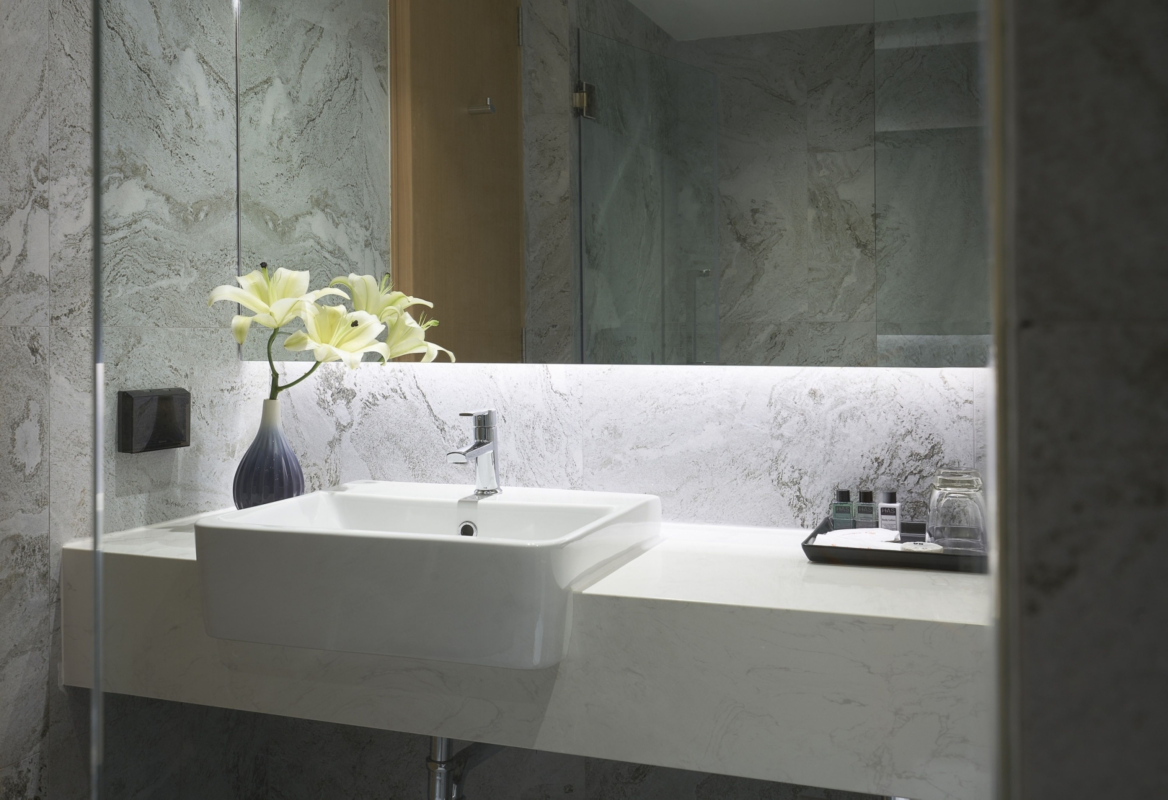 A modern bathroom with a white sink, a glass shower enclosure, and a vase with white flowers.