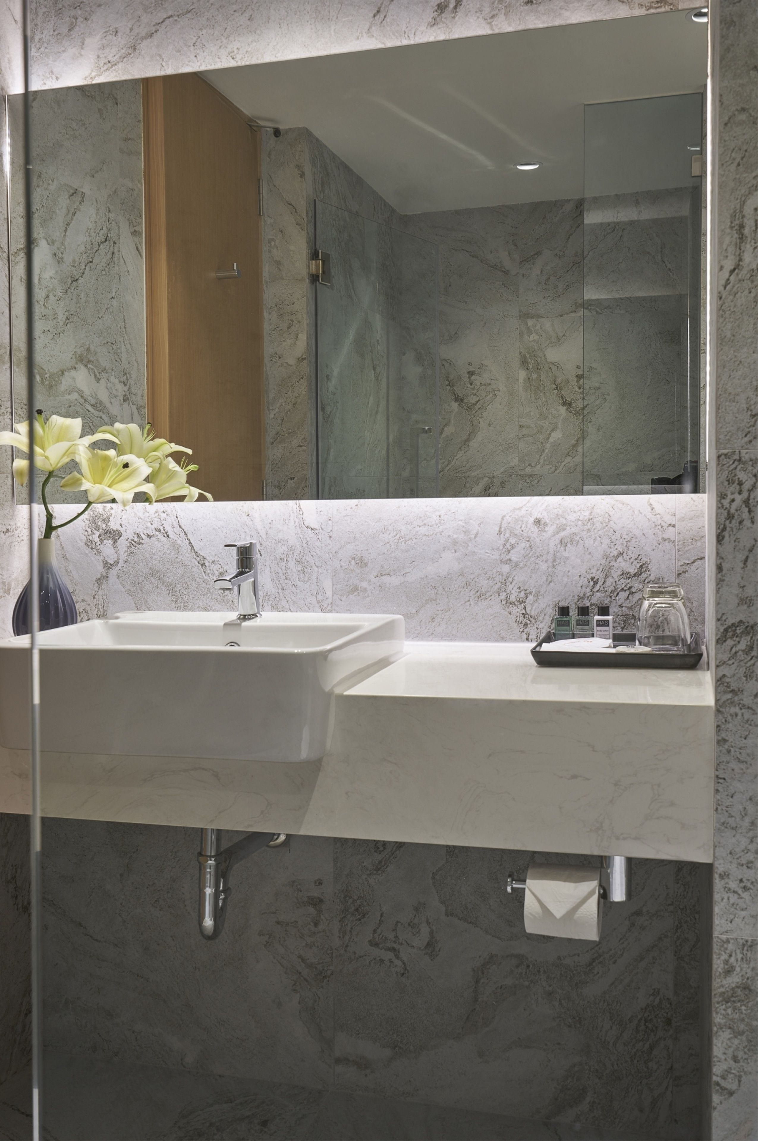 Un baño con lavamanos doble, espejo y un florero con flores.