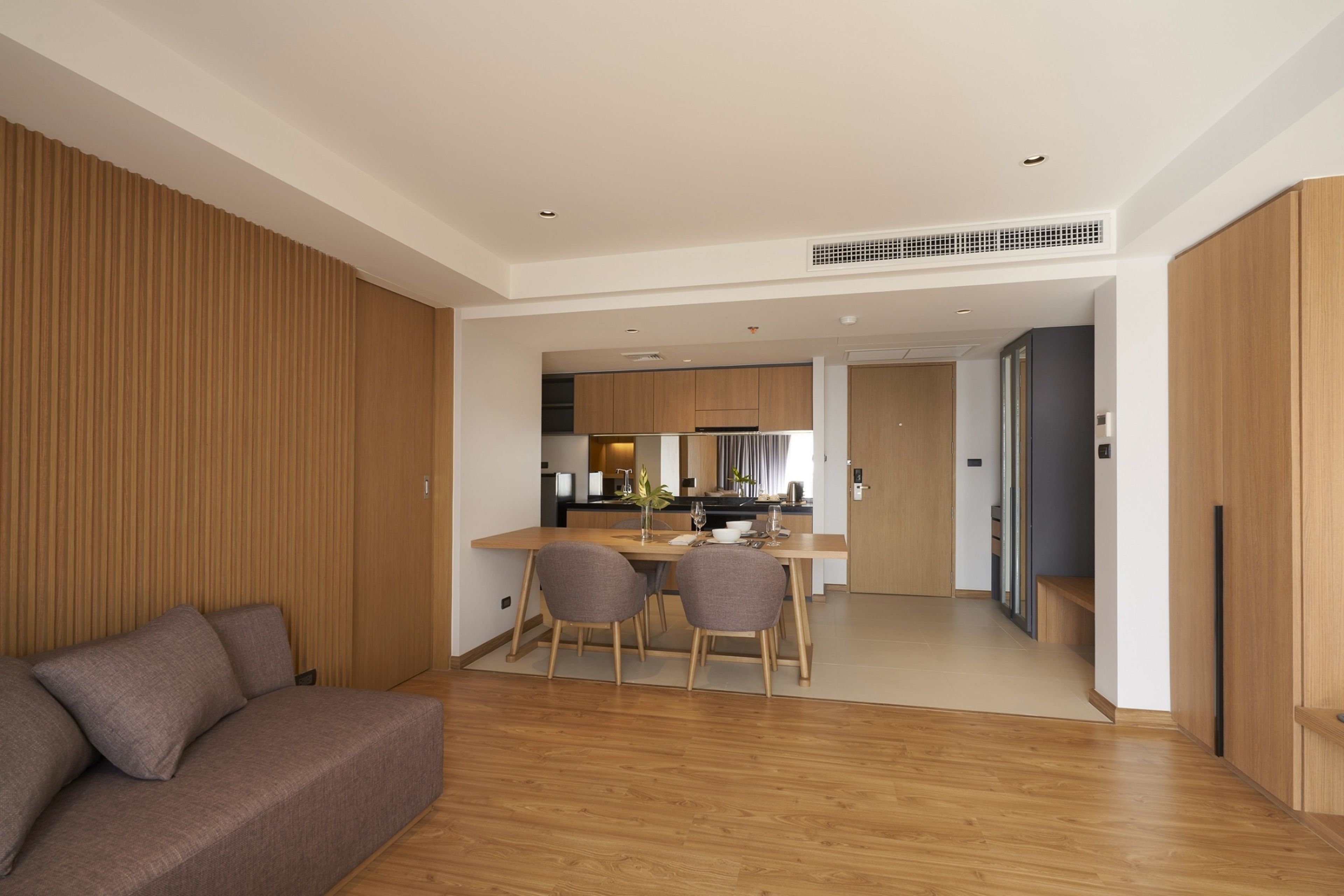 A modern living room with a sofa, dining table, and chairs. A kitchen area is visible in the background.