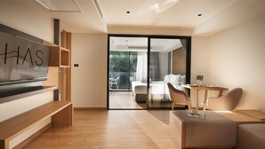 Een moderne woonkamer met een flatscreen televisie, houten meubels, een glazen deur naar een balkon, en een bordje met de tekst 