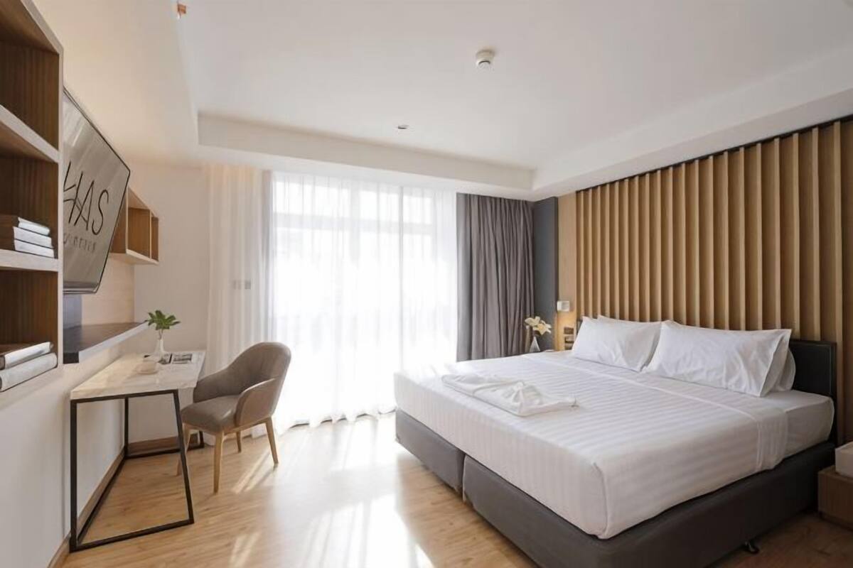 Une chambre d’hôtel avec un lit, un bureau, une chaise et une grande fenêtre.
