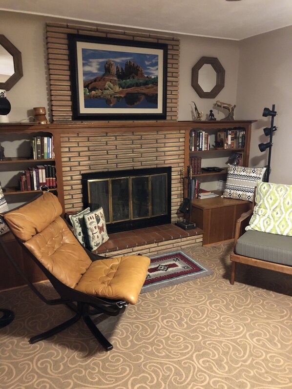 Una sala de estar con chimenea de ladrillo, sillón de cuero y sofá con cojines estampados.