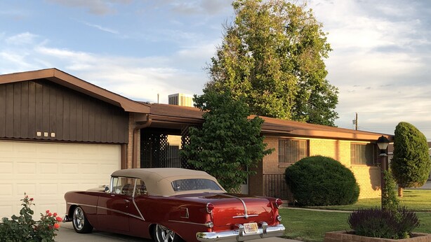 En röd, klassisk bil parkerad framför ett hus med ett garage.