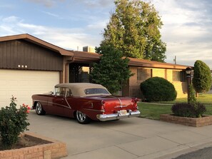 Un coche clásico rojo estacionado frente a una casa con garaje.