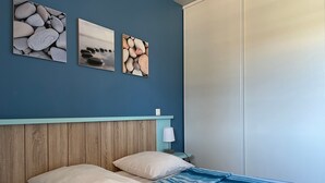Une chambre à coucher avec une tête de lit en bois, un lit recouvert d’une couvre-lit à rayures bleues et trois tableaux encadrés accrochés au mur.